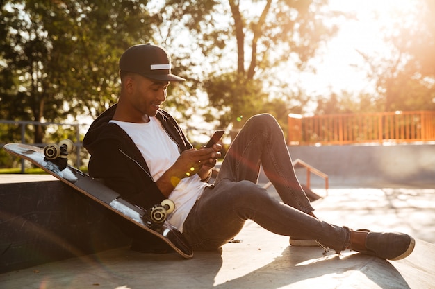 Jonge afrikaanse man met een skateboard met smartphone