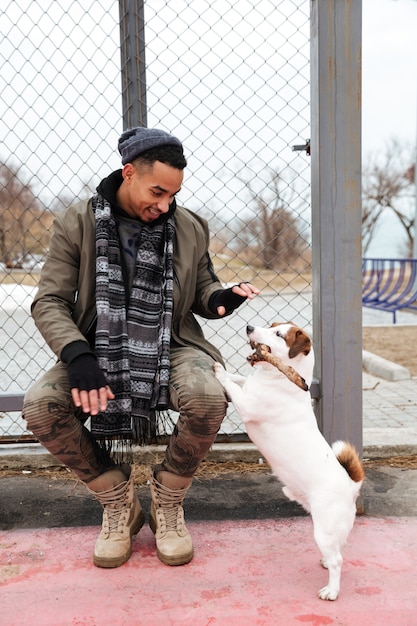 Gratis foto jonge afrikaanse man met muts en sjaal wandelen met hond.