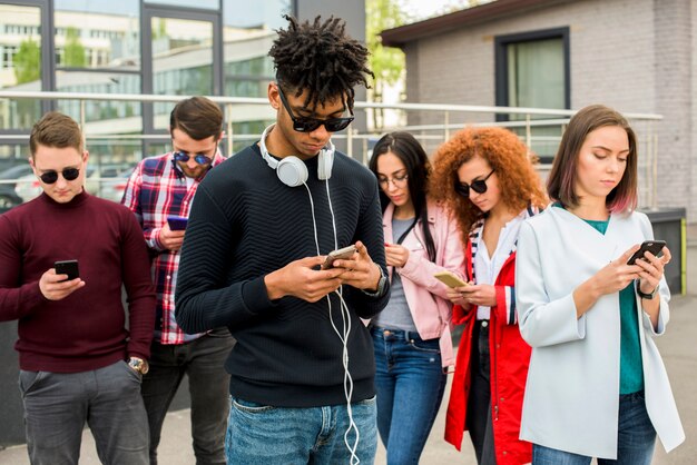 Jonge Afrikaanse mens die zich voor zijn vrienden bevindt die mobiele telefoons met behulp van