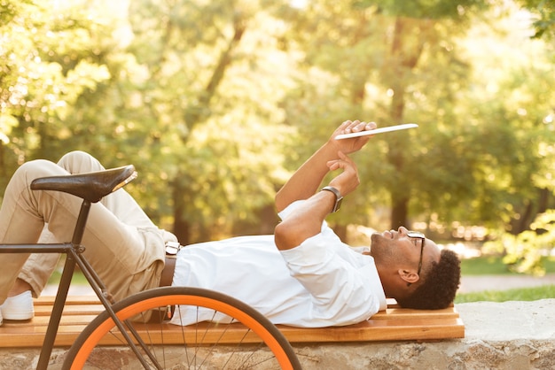 Gratis foto jonge afrikaanse mens vroege ochtend met fiets die in openlucht tablet gebruiken