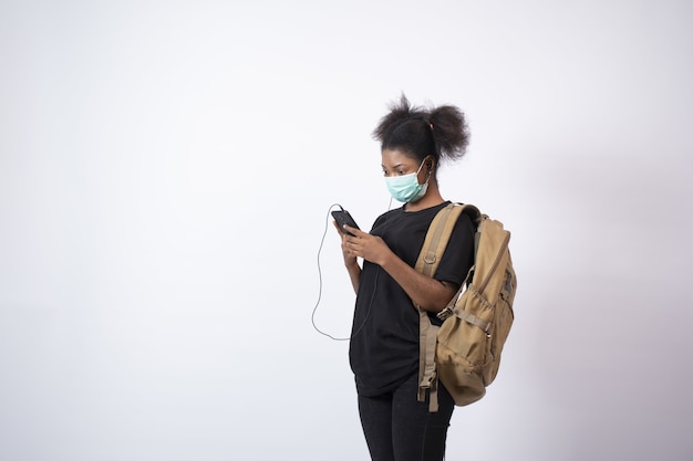 Jonge Afrikaanse vrouw die een gezichtsmasker draagt met haar mobiele telefoon