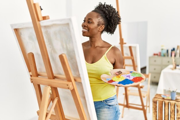 Jonge afro-amerikaanse kunstenaarsvrouw die lacht gelukkig tekenen in kunststudio.