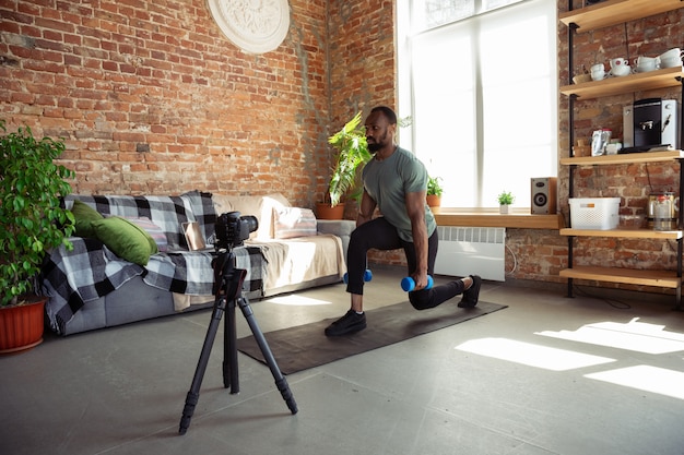 Jonge Afro-Amerikaanse man lesgeven thuis online cursussen van fitness, aërobe, sportieve levensstijl tijdens quarantaine, opname op camera, streaming