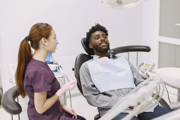 Jonge afro-amerikaanse man. man bezoekt het kantoor van de tandarts voor preventie van de mondholte. man en famale arts tijdens controle tanden.