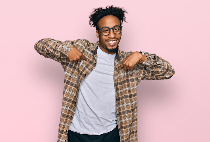 Gratis Foto jonge afro-amerikaanse man met baard, gekleed in casual kleding en een bril, zelfverzekerd met een glimlach op het gezicht, zichzelf wijzend met vingers trots en gelukkig.
