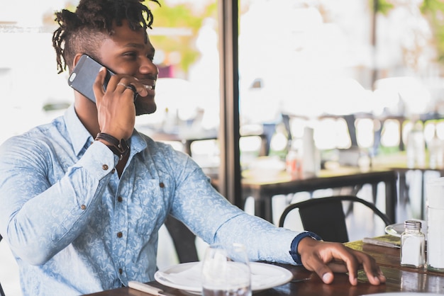 Jonge Afro-Amerikaanse man praten aan de telefoon terwijl hij in een restaurant zit.