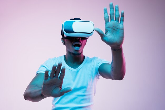 Jonge Afro-Amerikaanse man speelt en gebruikt VR-bril in neonlicht op verloop