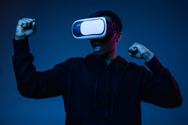 Jonge Afro-Amerikaanse man spelen in VR-bril in neonlicht op verloop achtergrond. Mannelijk portret