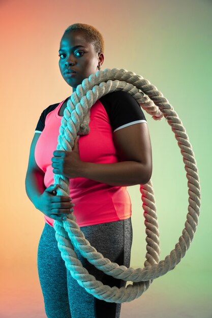 Jonge afro-amerikaanse plus size vrouwelijke model training op gradiënt muur in neonlicht.