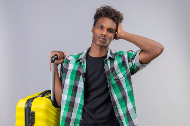 Jonge Afro-Amerikaanse reiziger man die met koffer camera kijken verward en erg angstig op witte achtergrond