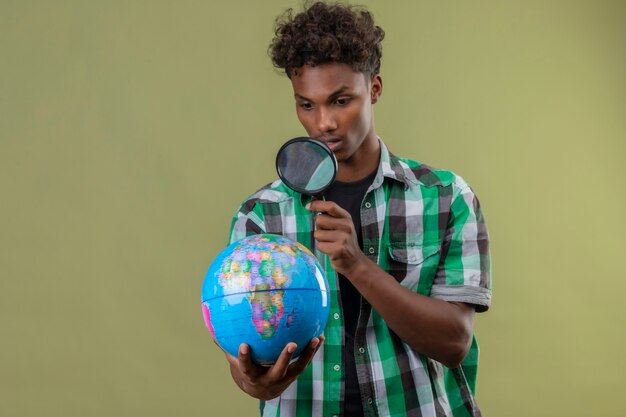 Jonge Afro-Amerikaanse reiziger man met globe kijken door vergrootglas verrast