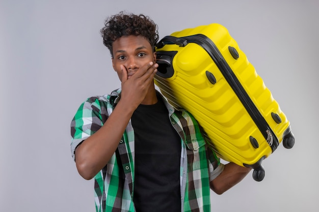 Jonge Afro-Amerikaanse reiziger man met koffer verrast en verbaasd over mond met hand