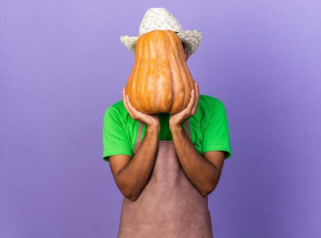 Jonge afro-amerikaanse tuinman met een tuinhoed en een bedekt gezicht met pompoen