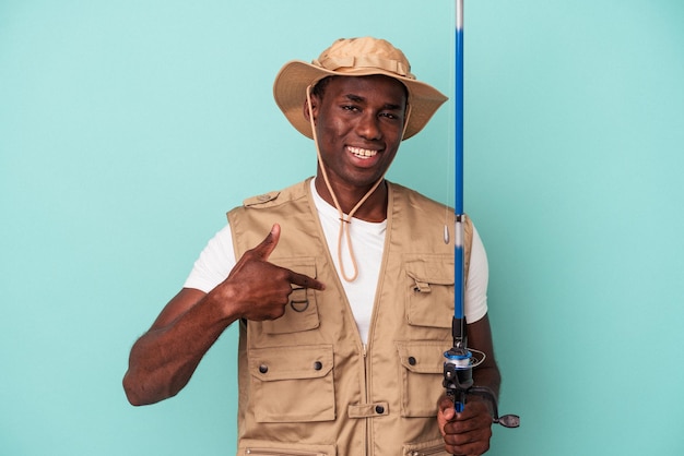 Jonge afro-amerikaanse visser met staaf geïsoleerd op blauwe achtergrond persoon die met de hand wijst naar een shirt kopieerruimte, trots en zelfverzekerd