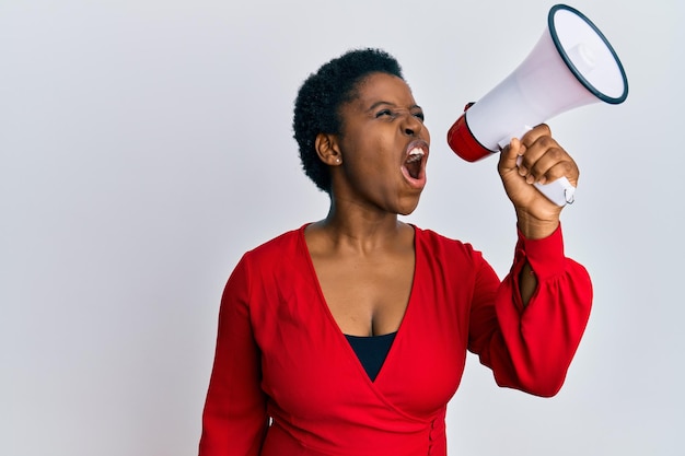 Jonge afro-amerikaanse vrouw die boos schreeuwt met behulp van een megafoon over een geïsoleerde witte achtergrond.
