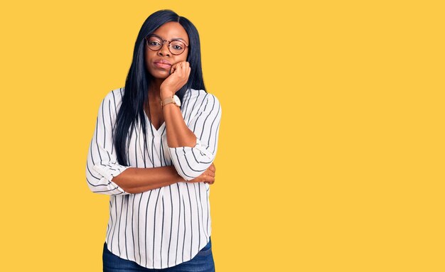 Jonge afro-amerikaanse vrouw die casual kleding en een bril draagt en denkt dat ze er moe en verveeld uitziet met depressieproblemen met gekruiste armen.