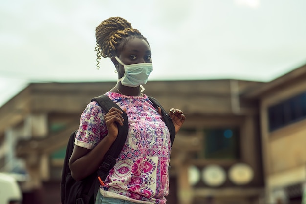 Jonge Afro-Amerikaanse vrouw die een beschermend gezichtsmasker draagt met een rugzak buitenshuis