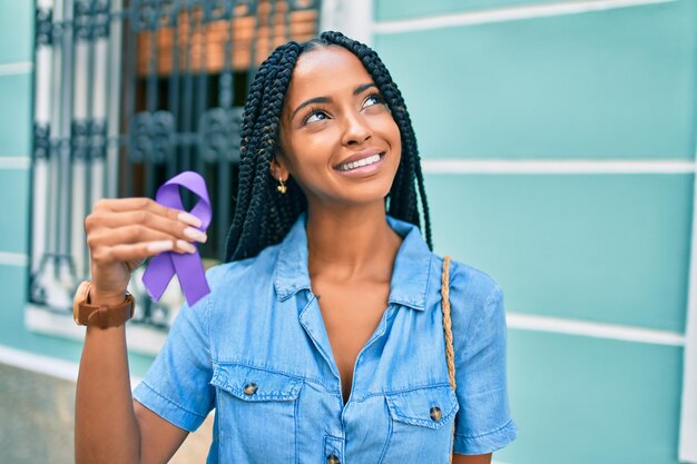 Jonge afro-amerikaanse vrouw die lacht gelukkig met paars lint wandelen in de stad