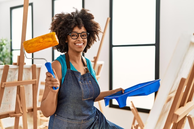 Jonge afro-amerikaanse vrouw die lacht zelfverzekerd tekenen met roller in kunststudio