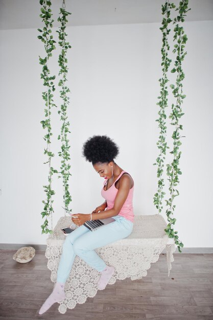 Jonge afro-amerikaanse vrouw die op de schommel zit terwijl ze op laptop werkt