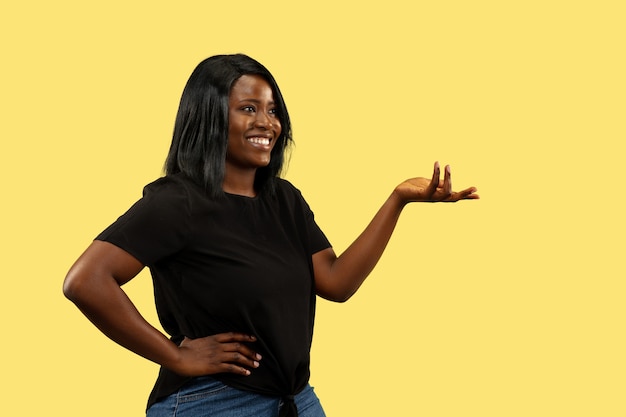 Jonge Afro-Amerikaanse vrouw geïsoleerd op gele studio achtergrond, gezichtsuitdrukking. Mooi vrouwelijk portret van halve lengte. Concept van menselijke emoties, gezichtsuitdrukking. Kiezen en uitnodigend.