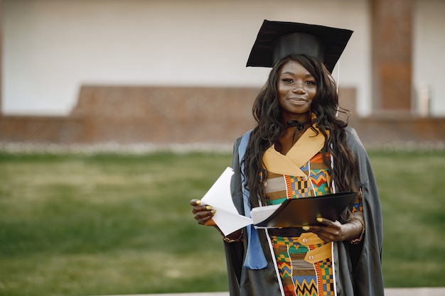 Jonge afro-amerikaanse vrouwelijke student gekleed in zwarte toga afstuderen. campus als achtergrond