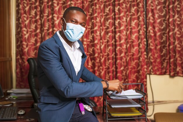 Jonge Afro-Amerikaanse zakenman draagt een beschermend masker in zijn kantoor