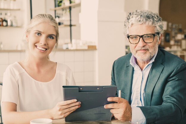 Jonge agent en volwassen klant ontmoeten elkaar tijdens een kopje koffie bij co-working, zittend aan tafel, met documenten