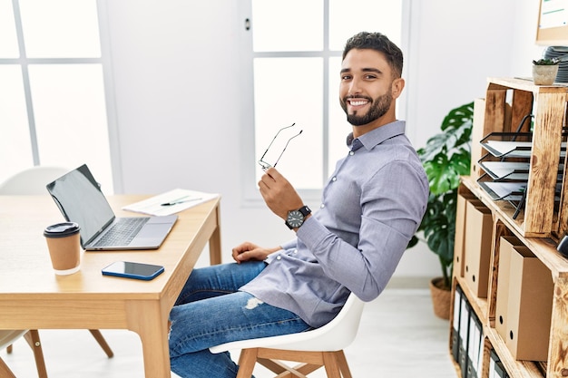 Jonge arabische man die lacht zelfverzekerd met behulp van laptop die op kantoor werkt