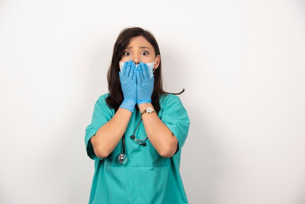 Jonge arts in medisch masker en handschoenen die haar gezicht op witte achtergrond houden. Hoge kwaliteit foto