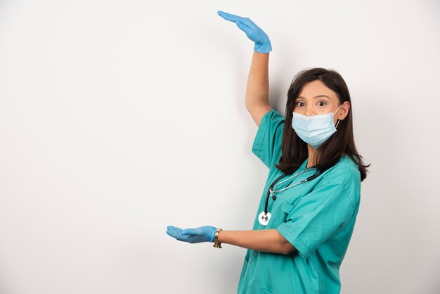 Jonge arts in medisch masker en handschoenen die open ruimte op witte achtergrond houden. Hoge kwaliteit foto