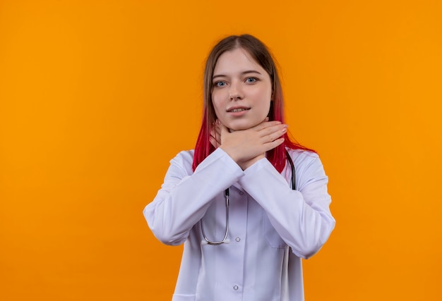 jonge artsenvrouw die stethoscoop medisch kleed draagt dat handen op keel op geïsoleerde oranje muur zet