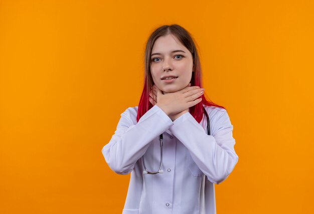 jonge artsenvrouw die stethoscoop medisch kleed draagt dat handen op keel op geïsoleerde oranje muur zet