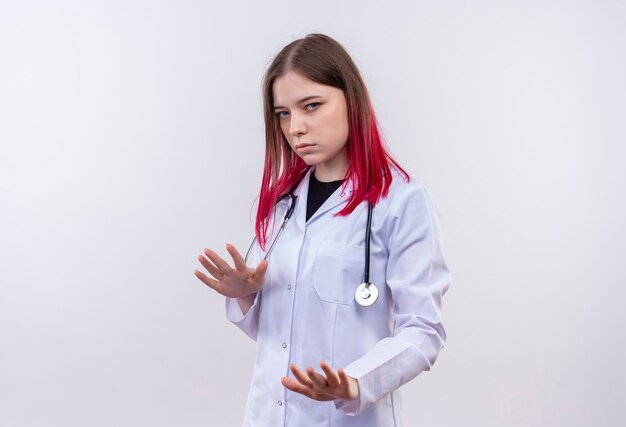 jonge artsenvrouw die stethoscoop medisch kleed draagt dat stopgebaar op geïsoleerde witte muur toont