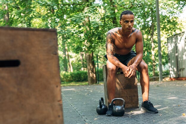 Jonge atleet rust tijdens training met kettlebells op het sportveld