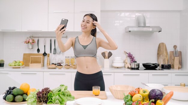 Jonge Aziatische bloggervrouw die zelf smartphone selfie in de keuken gebruikt