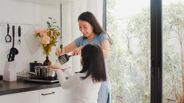 Jonge Aziatische Japanse moeder en dochter thuis koken. Levensstijlvrouwen gelukkig samen het maken van deegwaren en spaghetti voor ontbijtmaaltijd in moderne keuken bij huis in de ochtend.