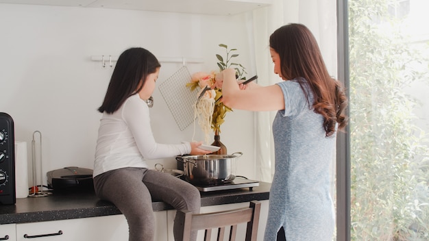 Jonge Aziatische Japanse moeder en dochter thuis koken. Levensstijlvrouwen gelukkig samen het maken van deegwaren en spaghetti voor ontbijtmaaltijd in moderne keuken bij huis in de ochtend.