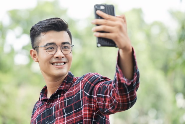 Jonge Aziatische man in glazen selfie buitenshuis te nemen