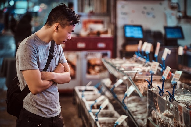 Jonge aziatische man kiest zeevruchten op de lokale chenise-markt. hij vergelijkt prijzen en zeevruchten.