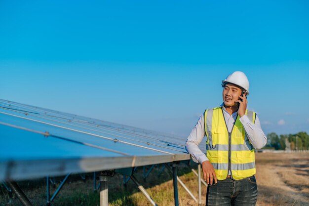 Jonge Aziatische technicus die op een smartphone staat en praat tussen lange rijen fotovoltaïsche zonnepanelen kopieert ruimte