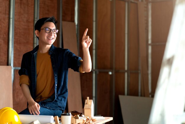 Jonge Aziatische timmerman hand tekenen in de lucht met copyspace voor uw tekst met achtergrond van huis renovatie site