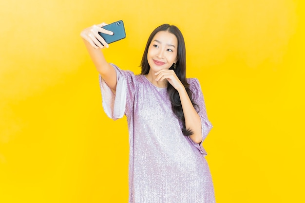jonge Aziatische vrouw die lacht met slimme mobiele telefoon op geel