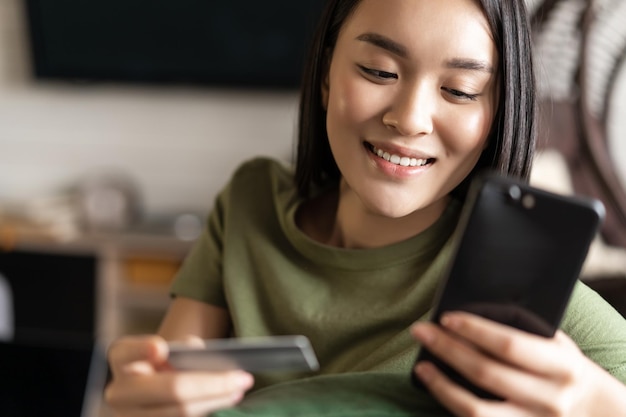 Jonge aziatische vrouw koopt van online winkel met behulp van mobiele telefoon en creditcard winkelen vanuit huis