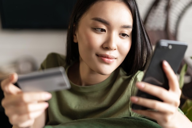 Jonge aziatische vrouw koopt van online winkel met behulp van mobiele telefoon en creditcard winkelen vanuit huis