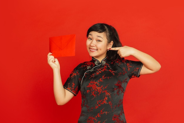 Jonge Aziatische vrouw met rode envelop die op rode muur wordt geïsoleerd
