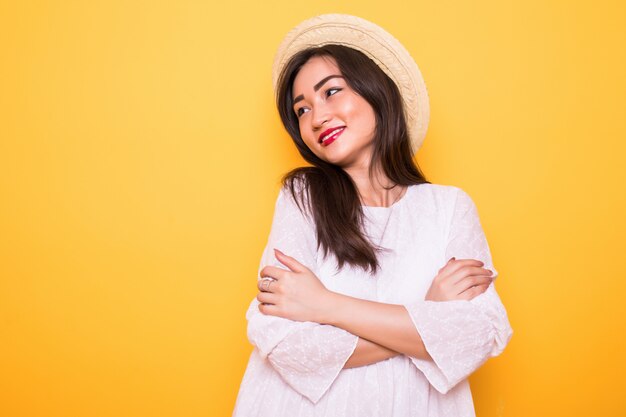 Jonge Aziatische vrouw met strohoed die op gele muur wordt geïsoleerd