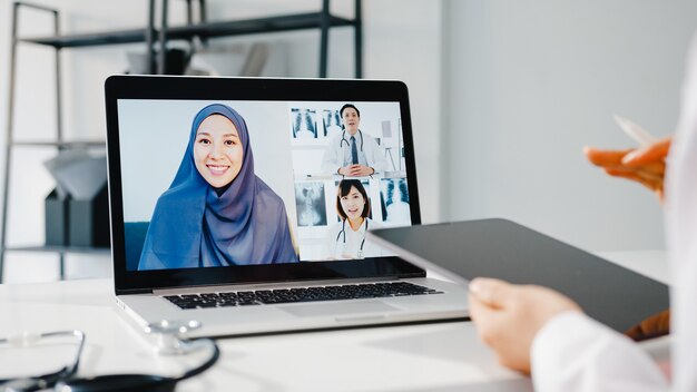 Jonge Aziatische vrouwelijke arts in wit medisch uniform met stethoscoop met behulp van computerlaptop die videoconferentiegesprek voert