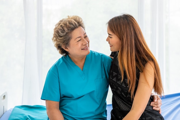 Jonge Aziatische vrouwelijke dochter bezoekt oudere, oudere vrouw, geduldige moeder in het ziekenhuis om de gezondheidszorg en het medische concept te ondersteunen en te motiveren