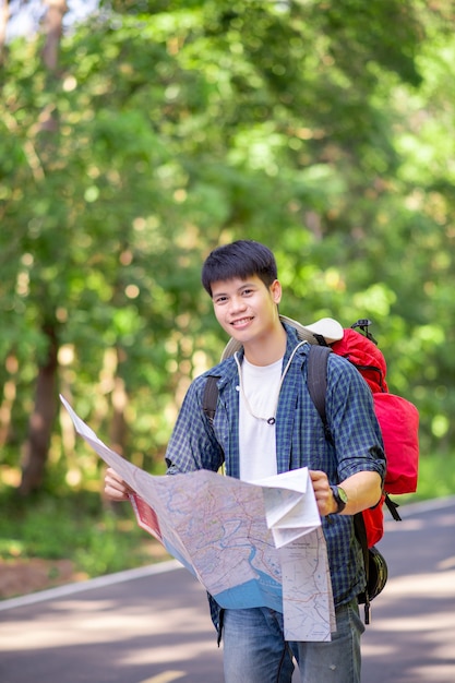 Jonge backpacker man reiziger met kaart, hij draagt grote rugzak tijdens het ontspannen buiten op zomervakanties in bosproef, kopieer ruimte